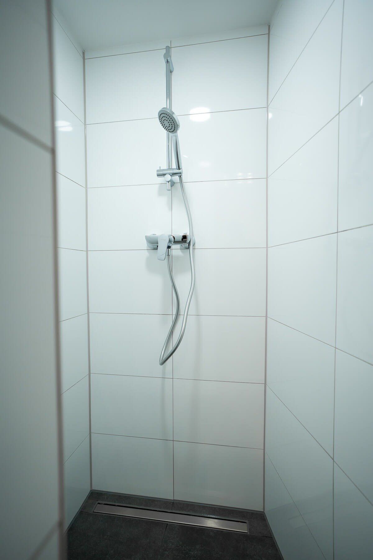 A shower with a handheld showerhead and a wall-mounted faucet.