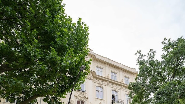 Un immeuble à plusieurs étages, de style architectural classique, avec des voitures garées dans la rue et un panneau indiquant qu’il est interdit de se garer.