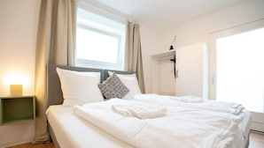 Un lit bien fait, avec du linge de lit blanc, une table de chevet avec une lampe et une fenêtre avec des rideaux.
