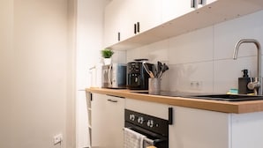 Une cuisine compacte avec des meubles blancs, un four encastré, un four à micro-ondes et un évier.