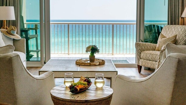 A room with a view of the ocean, a round table with a fruit bowl and glasses, and two chairs facing the view. - ☀️🌊 🏖️Stunning 5 Star Gulf Front 5th Floor, Regency Building 🌊☀️🏖️ (Navarre)