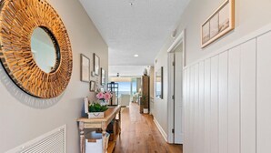A hallway with a round mirror, a wooden table with flowers, and a view to the outside. - ☀️🌊 🏖️Stunning 5 Star Gulf Front 5th Floor, Regency Building 🌊☀️🏖️ (Navarre)