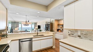A modern kitchen with white cabinetry, a central island with a sink, and a view to the living area. - ☀️🌊 🏖️Stunning 5 Star Gulf Front 5th Floor, Regency Building 🌊☀️🏖️ (Navarre)