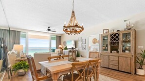 A dining area with a wooden table and chairs, a chandelier, and a view of the ocean. - ☀️🌊 🏖️Stunning 5 Star Gulf Front 5th Floor, Regency Building 🌊☀️🏖️ (Navarre)