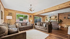 Ein gemütliches Wohnzimmer mit Holzwänden und -böden, zwei Sofas mit Karokissen, einer Kristallleuchter und einem Kamin.
