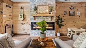 Ein gemütliches Wohnzimmer mit Kamin, Holzwänden, einer Gitarre und einem Essbereich.