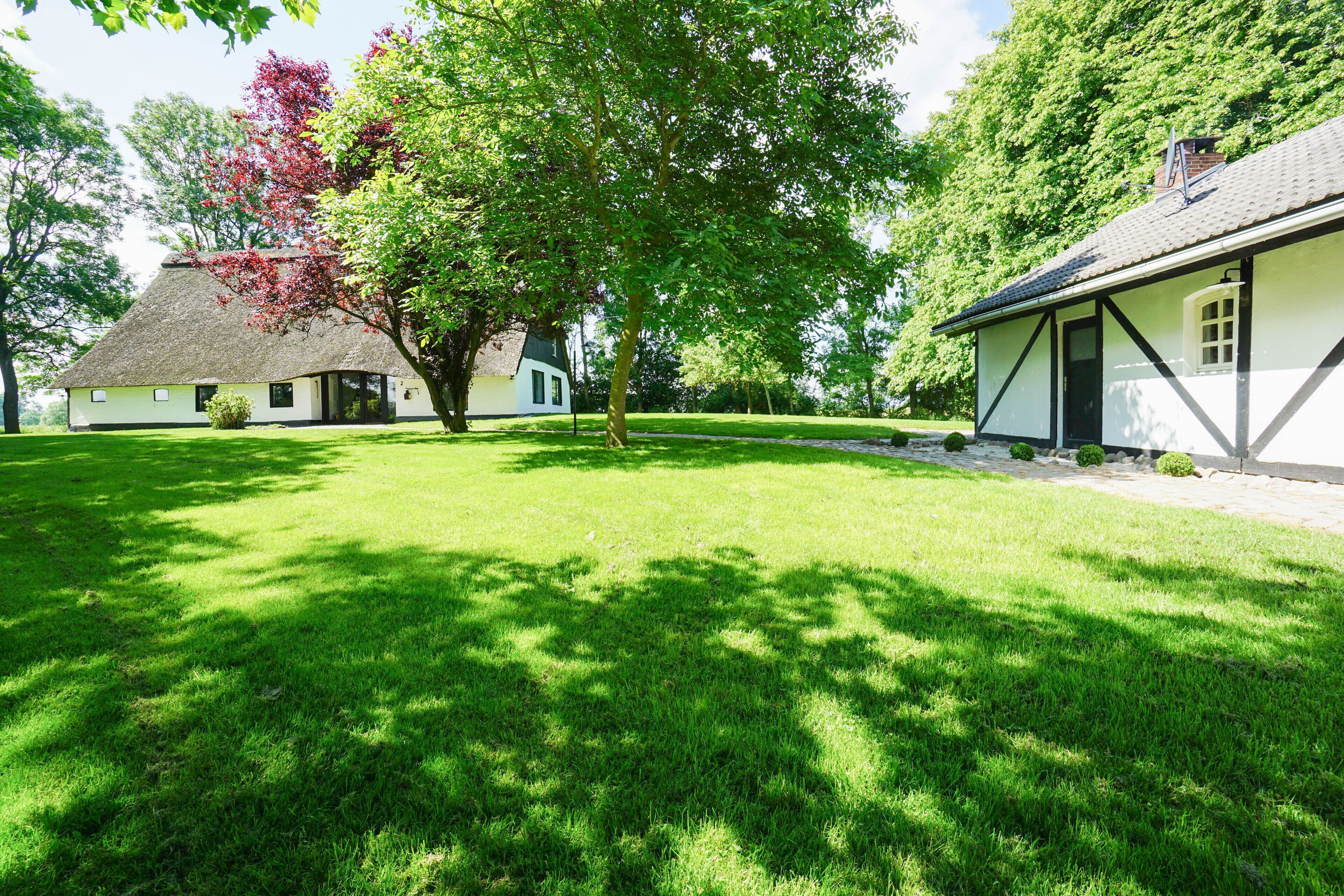 A traditional house with a thatched roof, surrounded by a well-maintained lawn and trees.