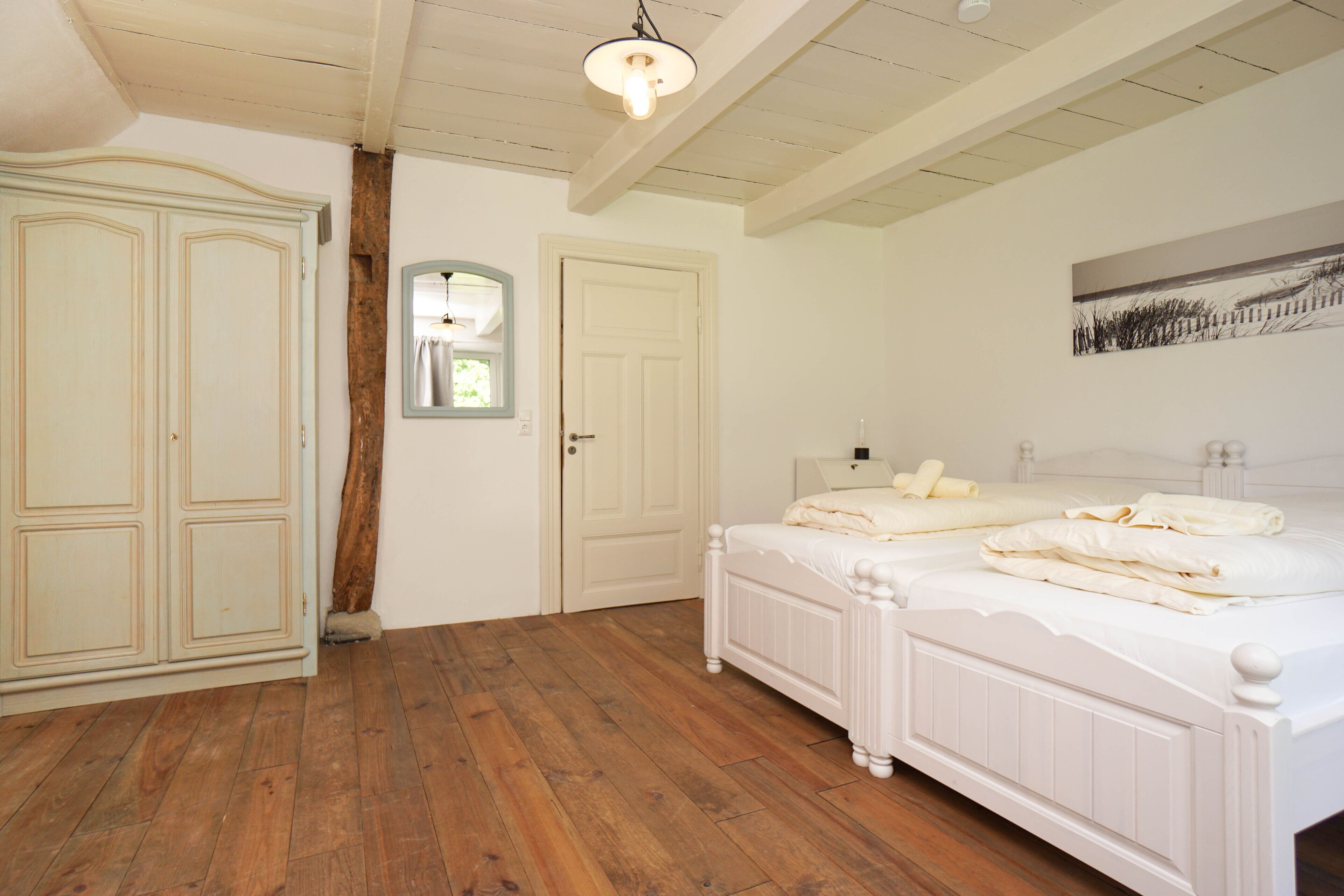 Un dormitorio con suelo de madera, una cama blanca con ropa de cama, un armario y un cuadro en la pared.