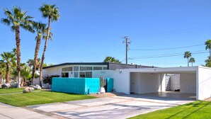 Une maison moderne avec un garage, une pelouse bien entretenue et de grands palmiers.