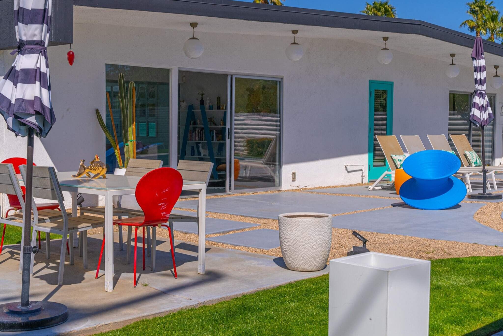 Un área de estar moderna al aire libre con una mesa y sillas, una maceta grande y un espacio de relajación junto a la piscina con tumbonas.