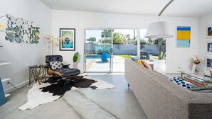 Un salon moderne avec un canapé en cuir, un tapis en peau de vache et une porte en verre donnant sur un espace piscine.