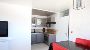 A compact kitchen with grey cabinets, a black sink, and a coffee maker. There is a dining area with a table and red chairs. - 300m from resort center, 3rd floor, terrace, balcony, tv, 29m², Chamrousse (Chamrousse)