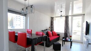 A modern living room with a black dining table, red chairs, a black sofa with red cushions, and a TV mounted on the wall. - 300m from resort center, 3rd floor, terrace, balcony, tv, 29m², Chamrousse (Chamrousse)