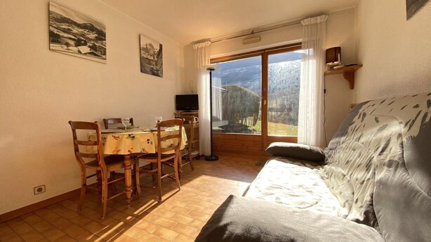 Une chambre avec un lit, une table à manger et des chaises, un téléviseur et une grande fenêtre donnant sur les montagnes.