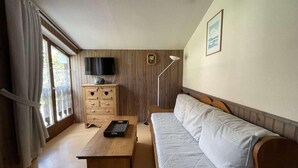 A room with a wooden sofa, a wooden table, a TV mounted on the wall, and a window with curtains.