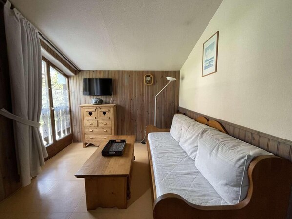 A room with a wooden sofa, a wooden table, a TV mounted on the wall, and a window with curtains.