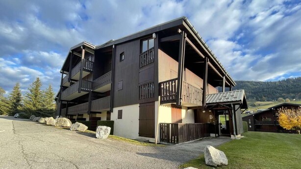 A two-story building with balconies, a gravel driveway, and a mountainous backdrop.