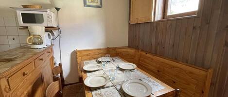 A wooden dining table set for four with plates, glasses, and cutlery. A microwave and kettle are on the counter.