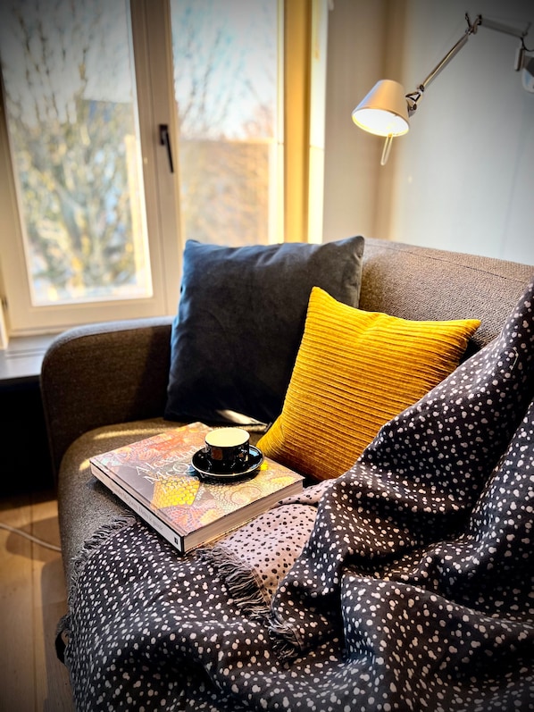 A cozy room with a window, a lamp, a book, and a cup on a cushion.