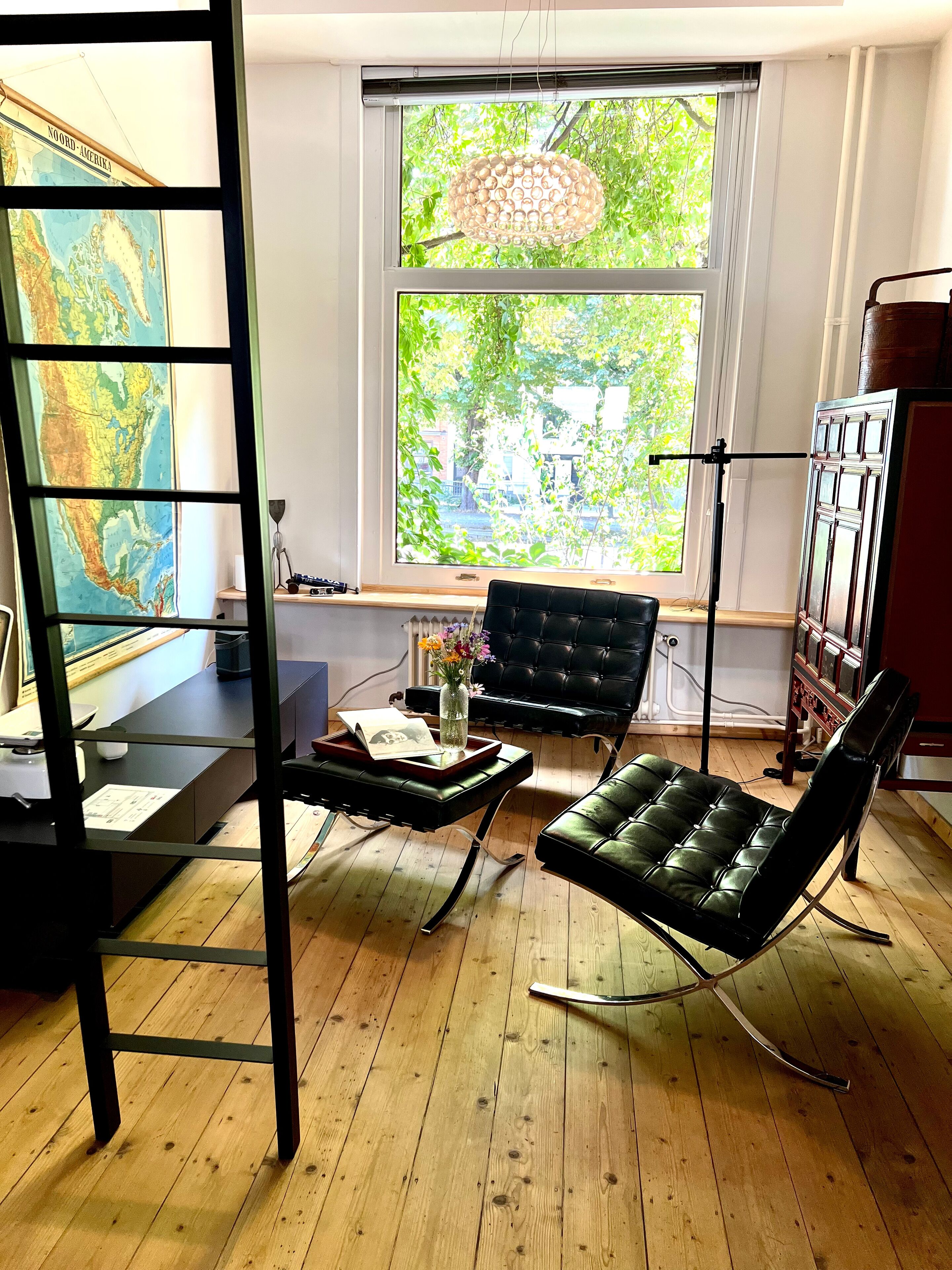 Une pièce avec une grande fenêtre, un fauteuil en cuir noir, un plancher en bois et une carte accrochée au mur.