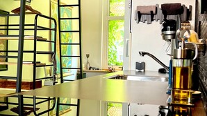 A bunk bed with a metal frame and a glass panel, a kitchen area with a sink and a coffee machine, and a view of a green outdoor area through a window. - Agelandkaai.be (Ghent)