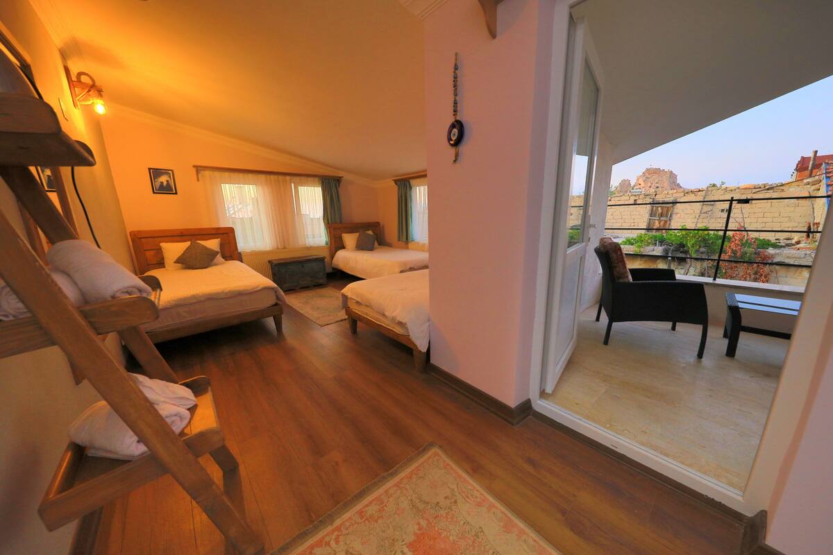 A hotel room with two beds, a wooden chair, a small table, and a balcony with a view of the city.