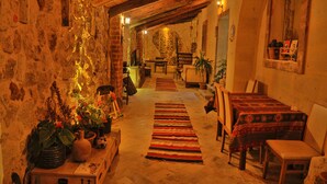 A cozy, rustic interior with a stone wall, wooden beams, and a long, striped rug leading to a dining area with tables and chairs.
