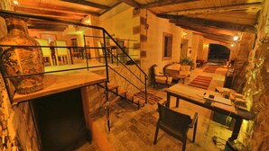 A rustic interior with a stone fireplace, wooden beams, a staircase, and a seating area with a table and chairs.