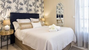 A bedroom with a large bed, a nightstand, a lamp, a mirror, and a window with curtains. - Penthouse Lorena Apartment (Granada)