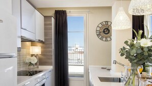 A modern kitchen with white cabinets, a black curtain, a clock, and a view of the balcony. - Penthouse Lorena Apartment (Granada)