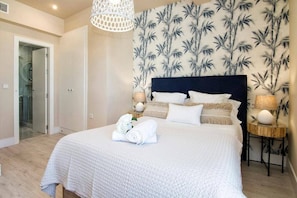Een slaapkamer met een groot bed, een hoofdbord, twee nachtkastjes met lampen, een wand met een bamboe blad patroon, en een deur naar een badkamer.