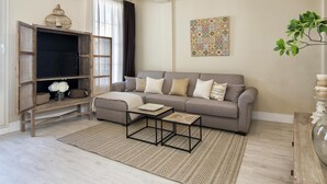 A living room with a grey sofa, a coffee table, a woven rug, a wooden cabinet, and a wall art piece. - Penthouse Lorena Apartment (Granada)