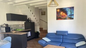 Un salon avec un canapé bleu, une table basse en bois, un coin cuisine équipé d’un four à micro-ondes et un escalier menant à un autre niveau.