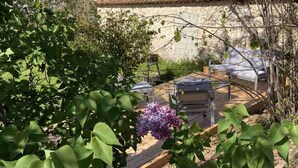 Un jardin agrémenté d’un bâtiment en pierre, d’une terrasse en bois et de plantes en fleurs.