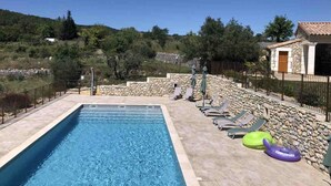 Une piscine entourée de murs et d’un bâtiment en pierre, avec des chaises longues et des bouées gonflables.