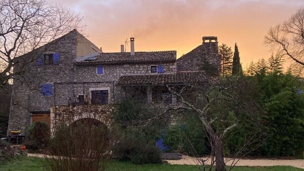 Un bâtiment en pierre, doté d’un toit en tuiles, entouré d’une pelouse et d’arbres.
