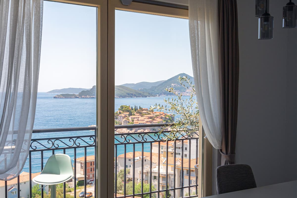 Un balcon avec une table et des chaises, une vue sur la mer et un paysage montagneux.