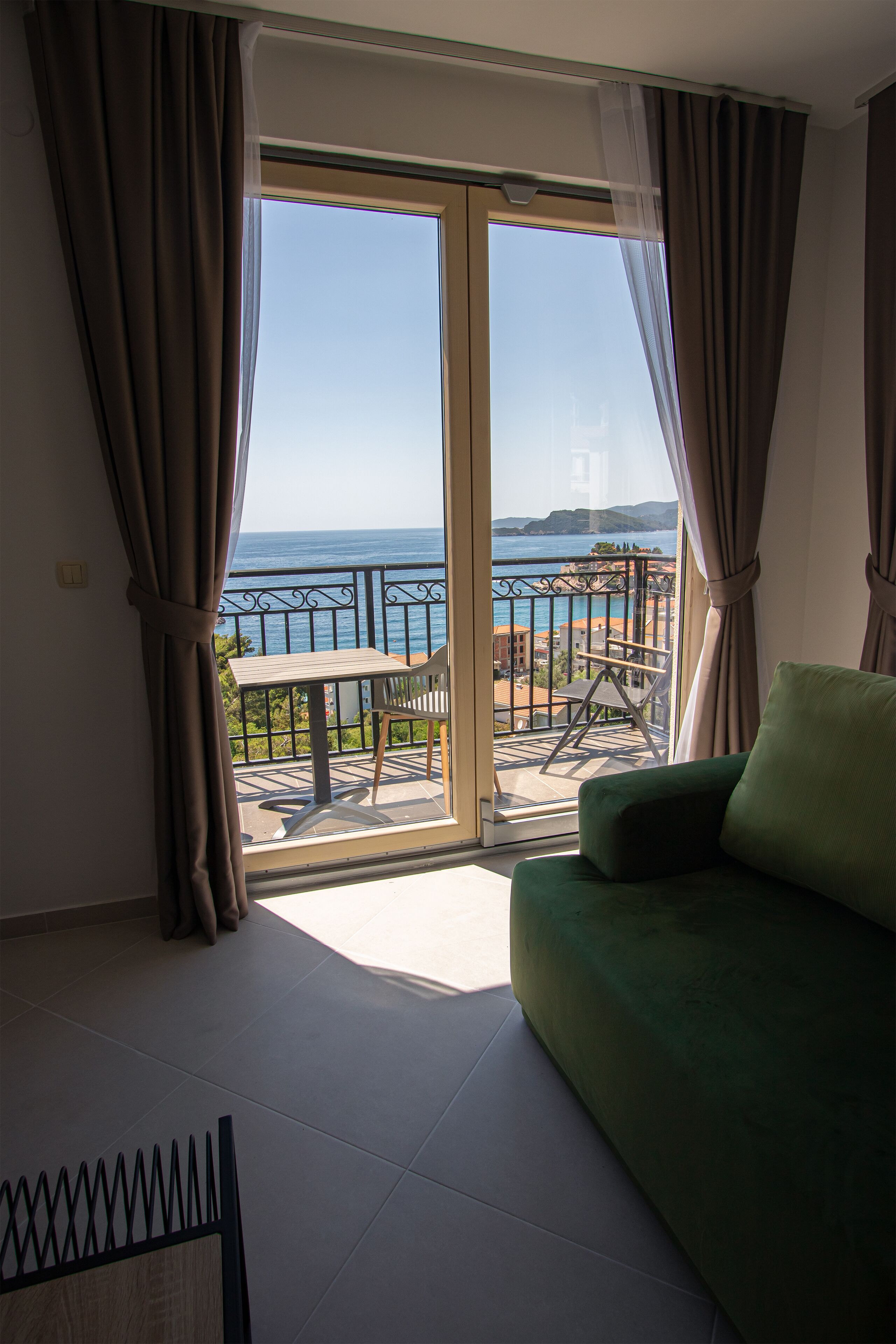 A balcony with a view of the sea, a green sofa, and a small table with chairs.
