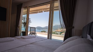 A hotel room with a large bed, a chair, and a view of the sea and mountains. - Vertmont Villa (Sveti Stefan)