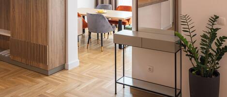 Un interior moderno con piso de madera, una zona de comedor con mesa y sillas, un espejo grande y una planta en maceta.