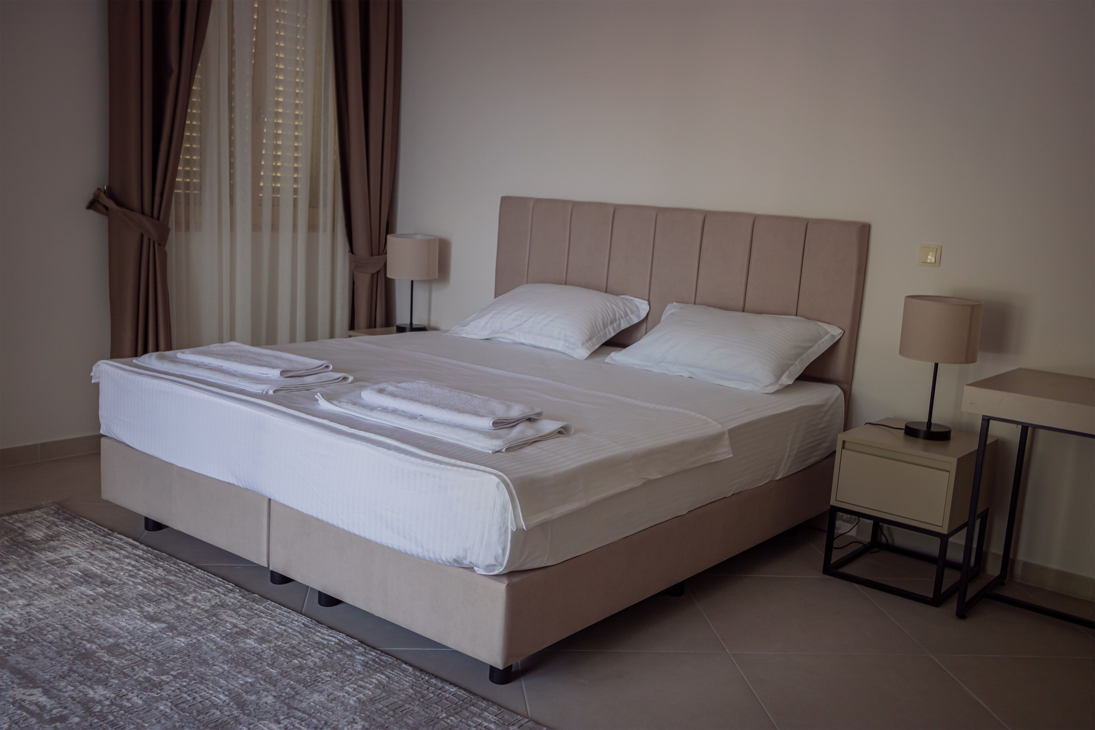 A neatly made bed with white linens and towels, a bedside table with a lamp, and a modern bedside console.