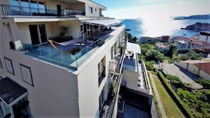 A modern multi-story building with a glass balcony overlooking a coastal area. - Vertmont Villa (Sveti Stefan)