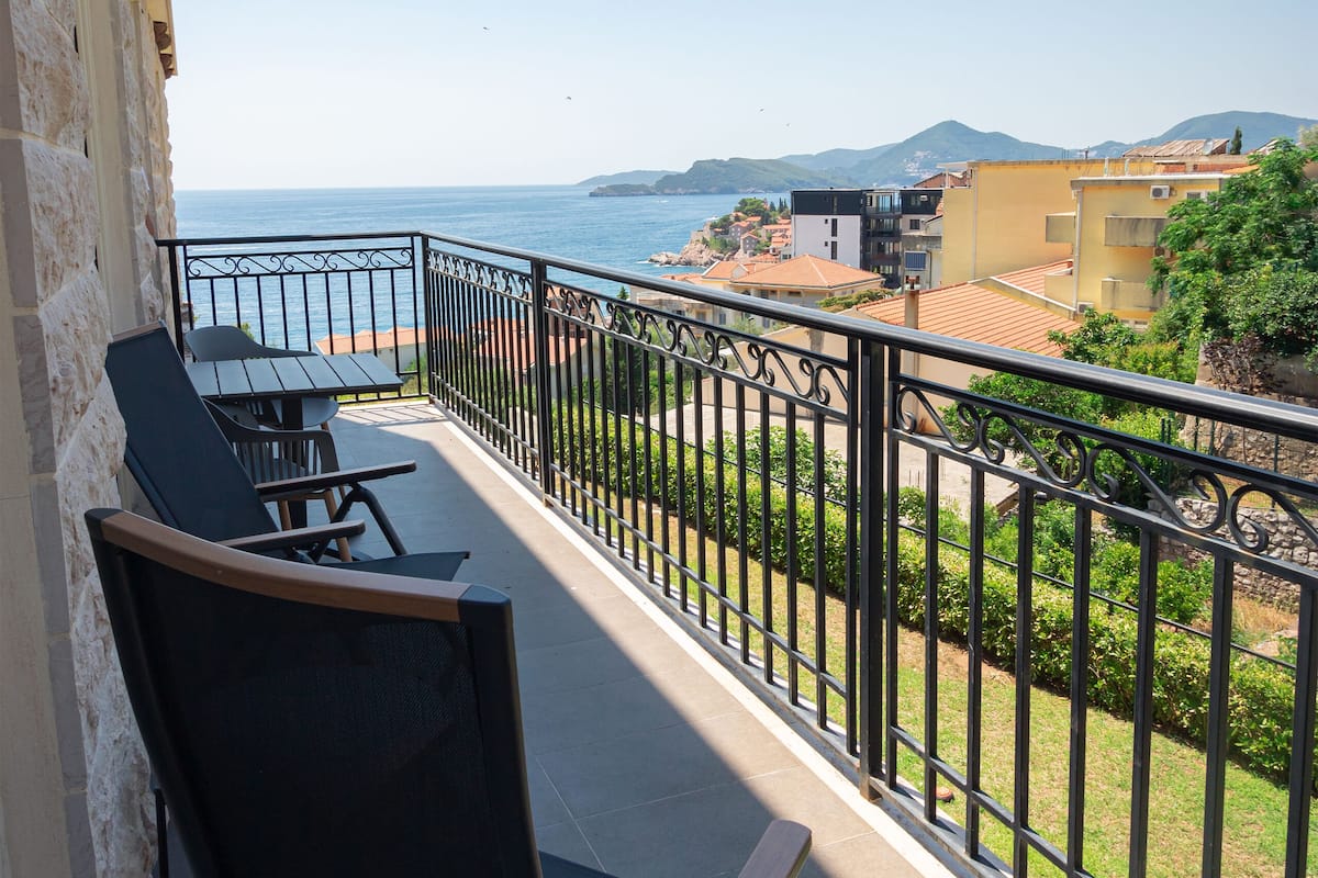 Un balcon avec une table et des chaises, offrant une vue sur la côte, avec des bâtiments et de la végétation.