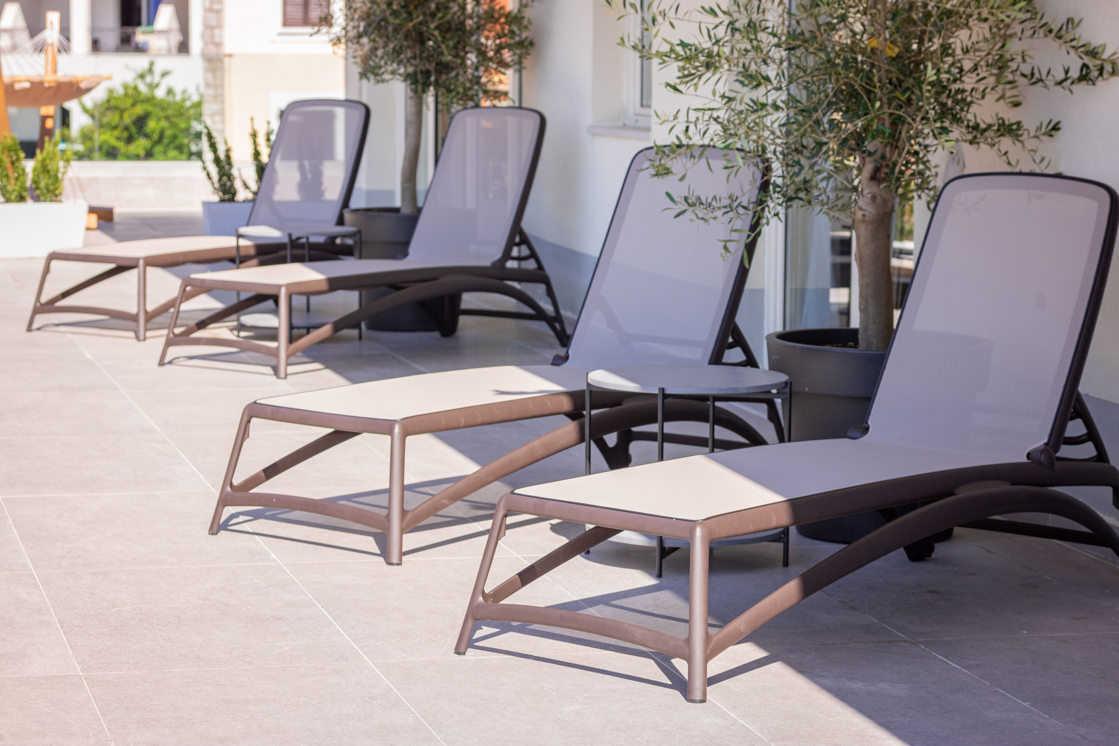 Outdoor lounge chairs with metal frames and cushioned seats, arranged on a tiled patio area.