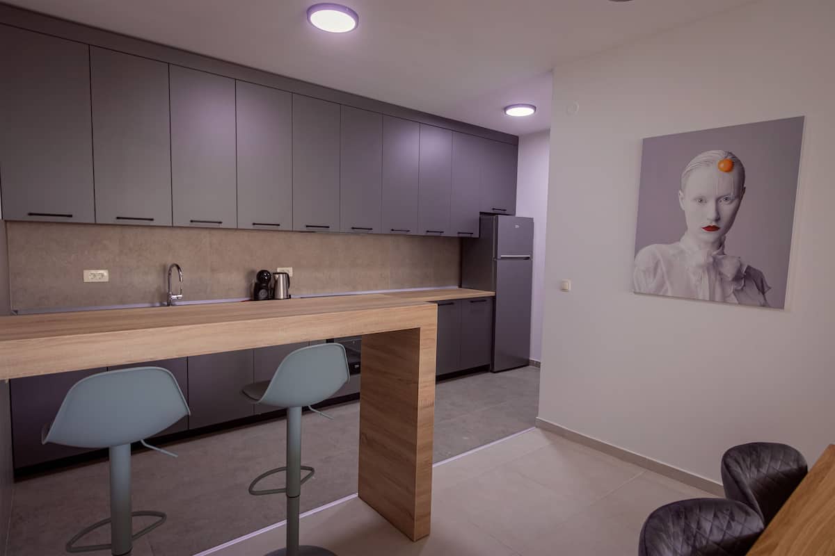 Une cuisine moderne avec des meubles gris, un plan de travail en bois et deux tabourets de bar.
