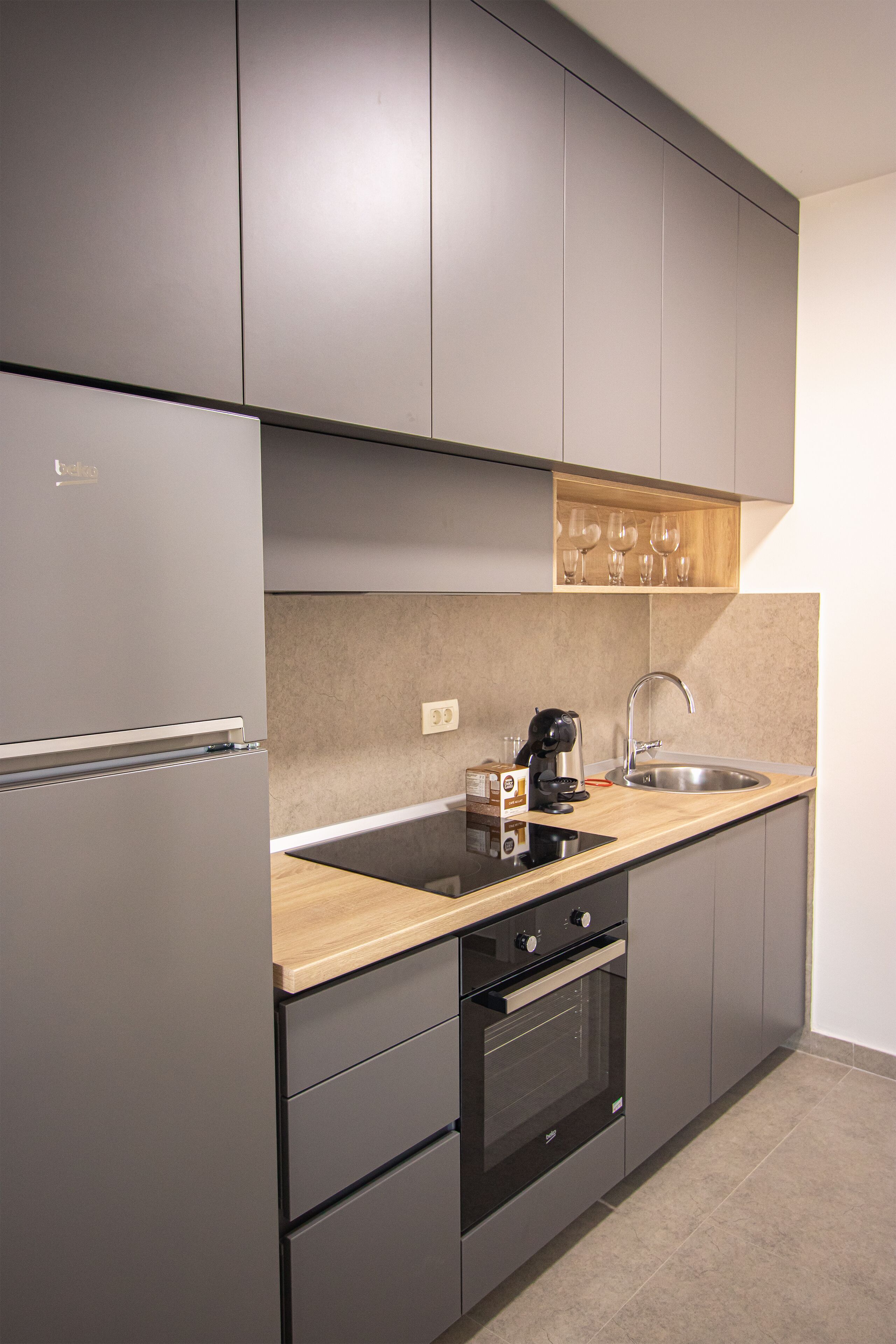 A modern kitchen with grey cabinets, a wooden countertop, a built-in oven, and a stainless steel sink.