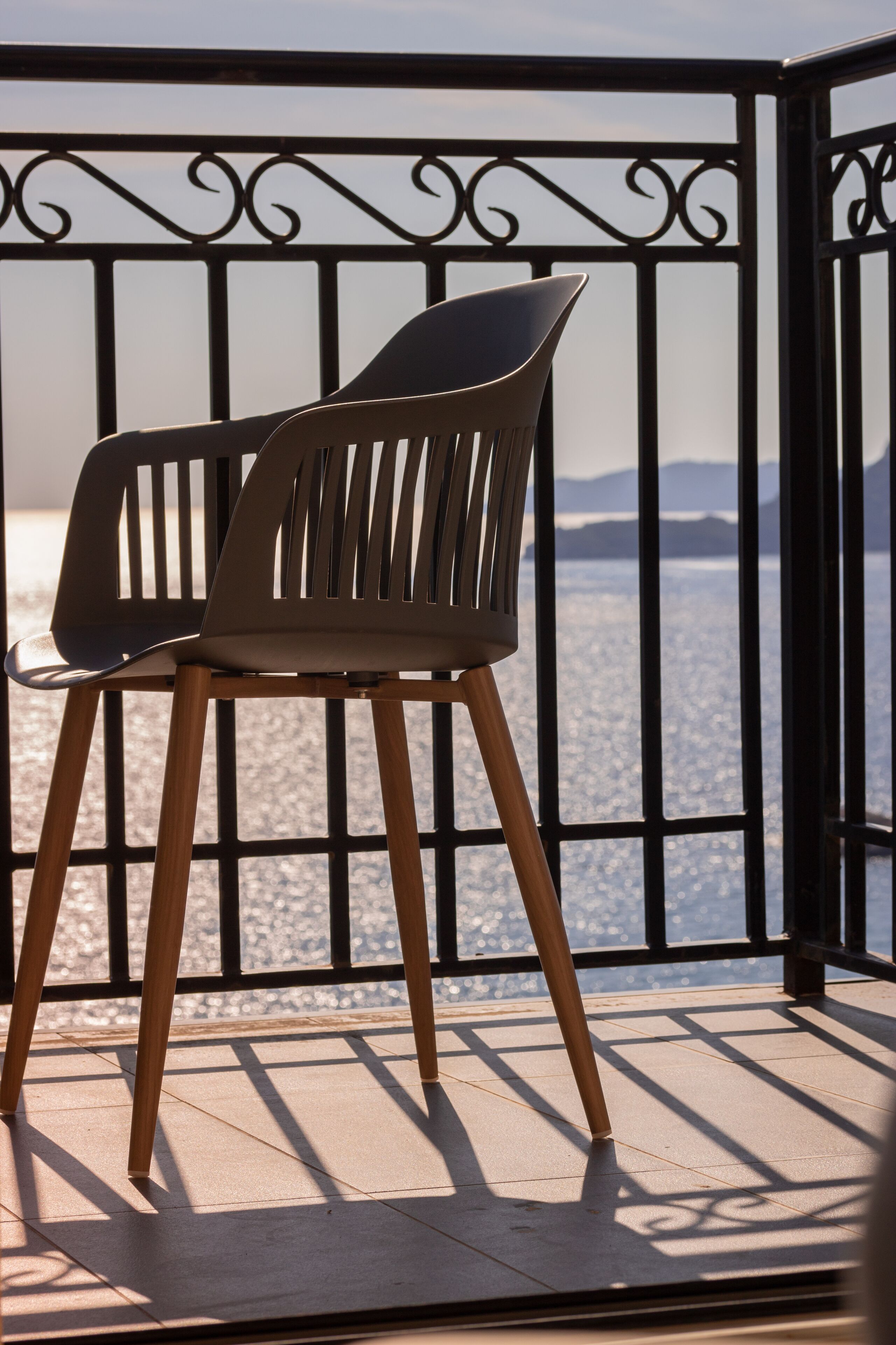 A modern chair with a slatted backrest and wooden legs, positioned on a balcony with a metal railing.