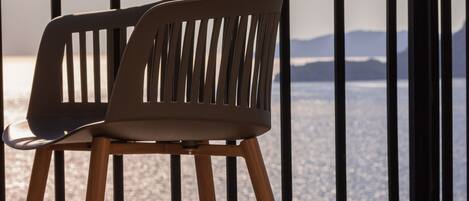 A modern chair with a slatted backrest and wooden legs, positioned on a balcony with a metal railing.