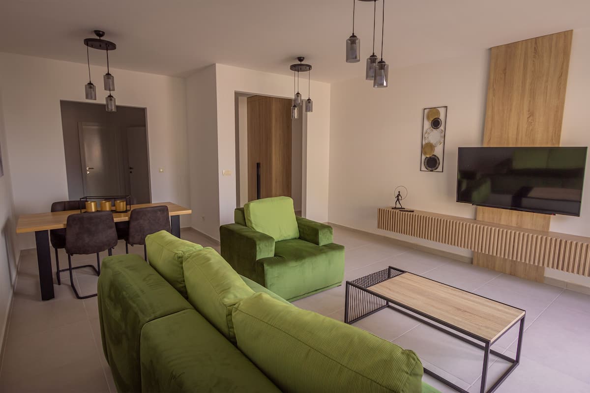 Un salon moderne avec des canapés verts, une table basse en bois et un téléviseur fixé au mur.