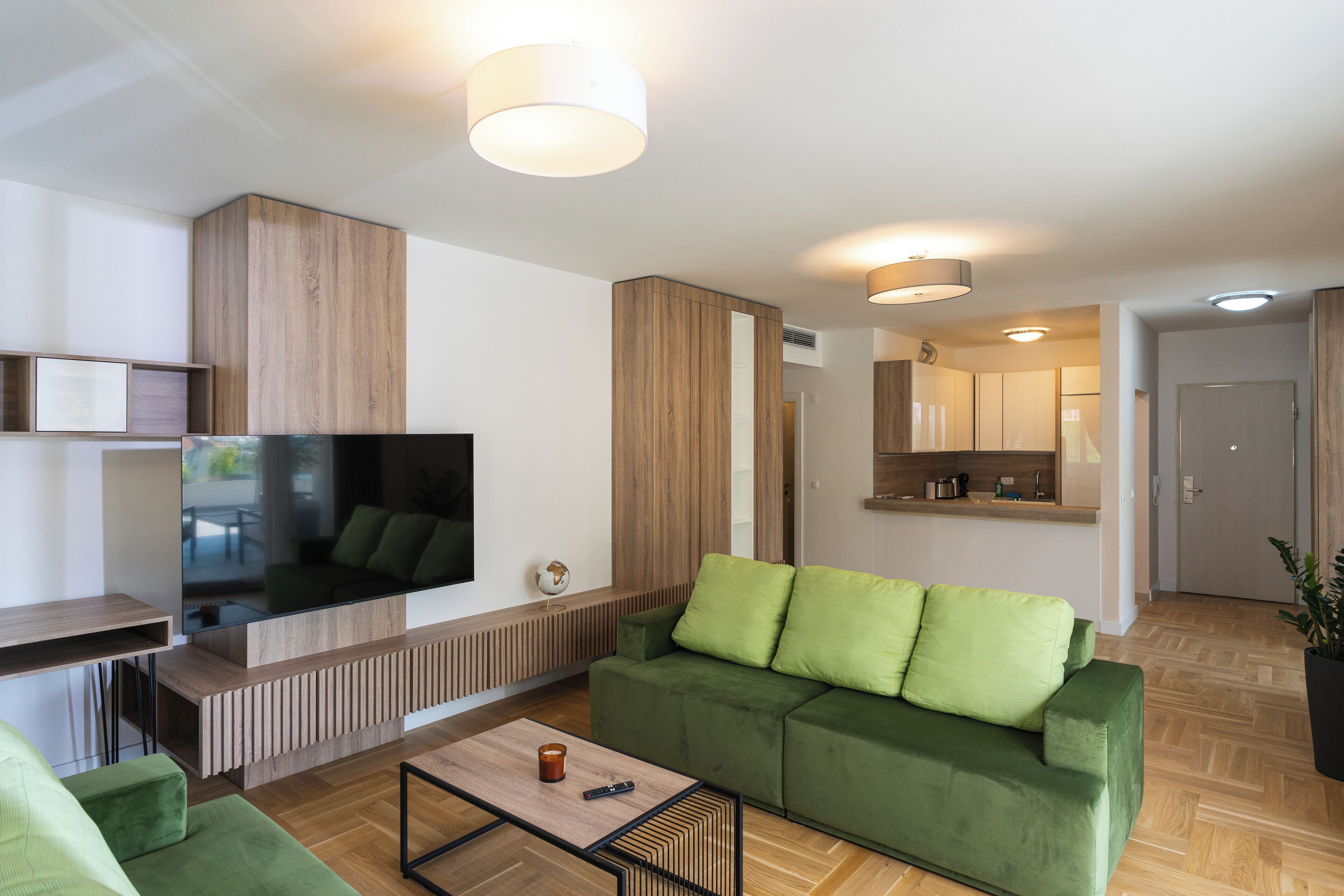 Een moderne woonkamer met een groene bank, een salontafel en een flatscreen televisie.